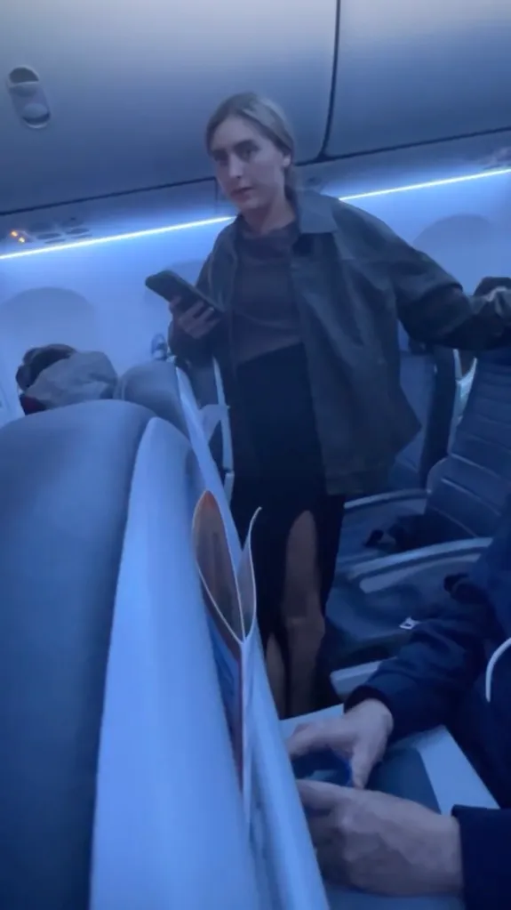 A woman standing on an airplane holding a phone.
